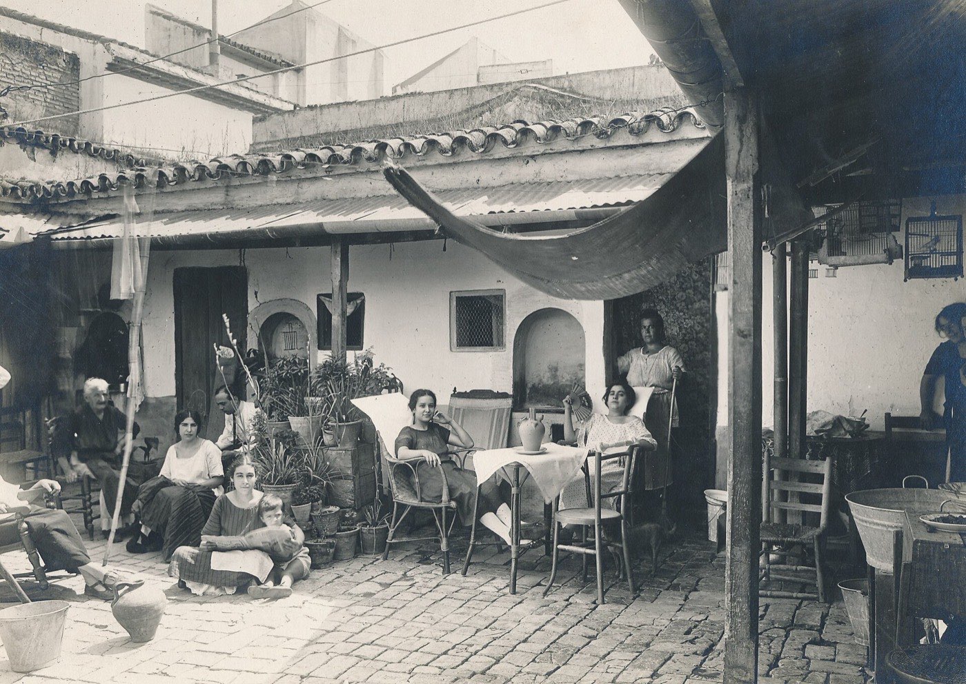 Vecinas y vecinos sentados juntos en el patio empedrado de una casa de vecinos de Sevilla